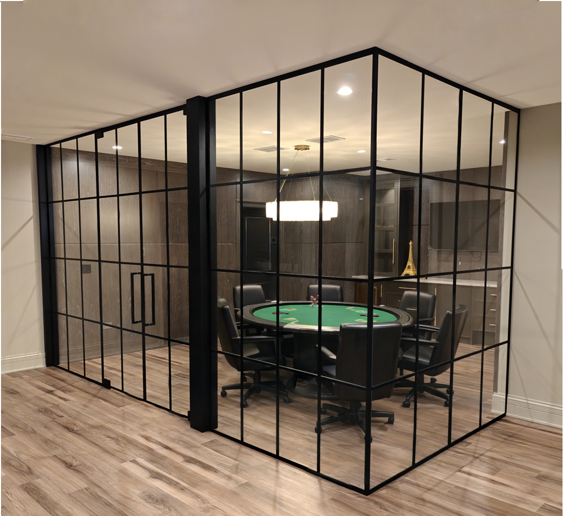 Black grid glass walls and double doors enclosing a game room, with wood flooring and a round table inside.