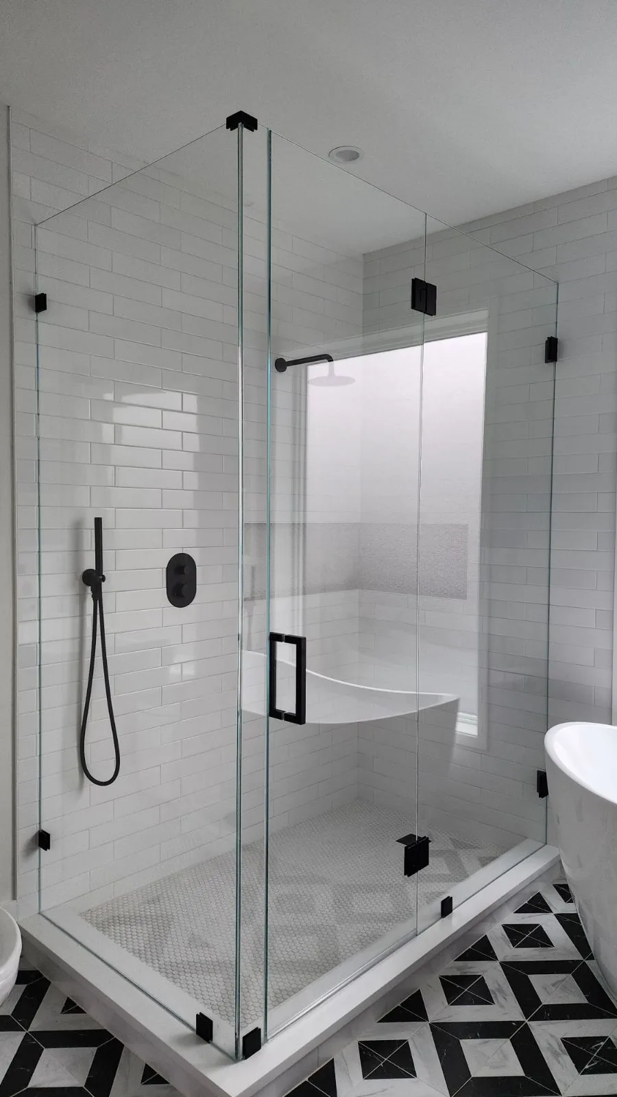 Clear shower enclosure with black hinges and handle, white rectangular wall tile and a geometric floor.