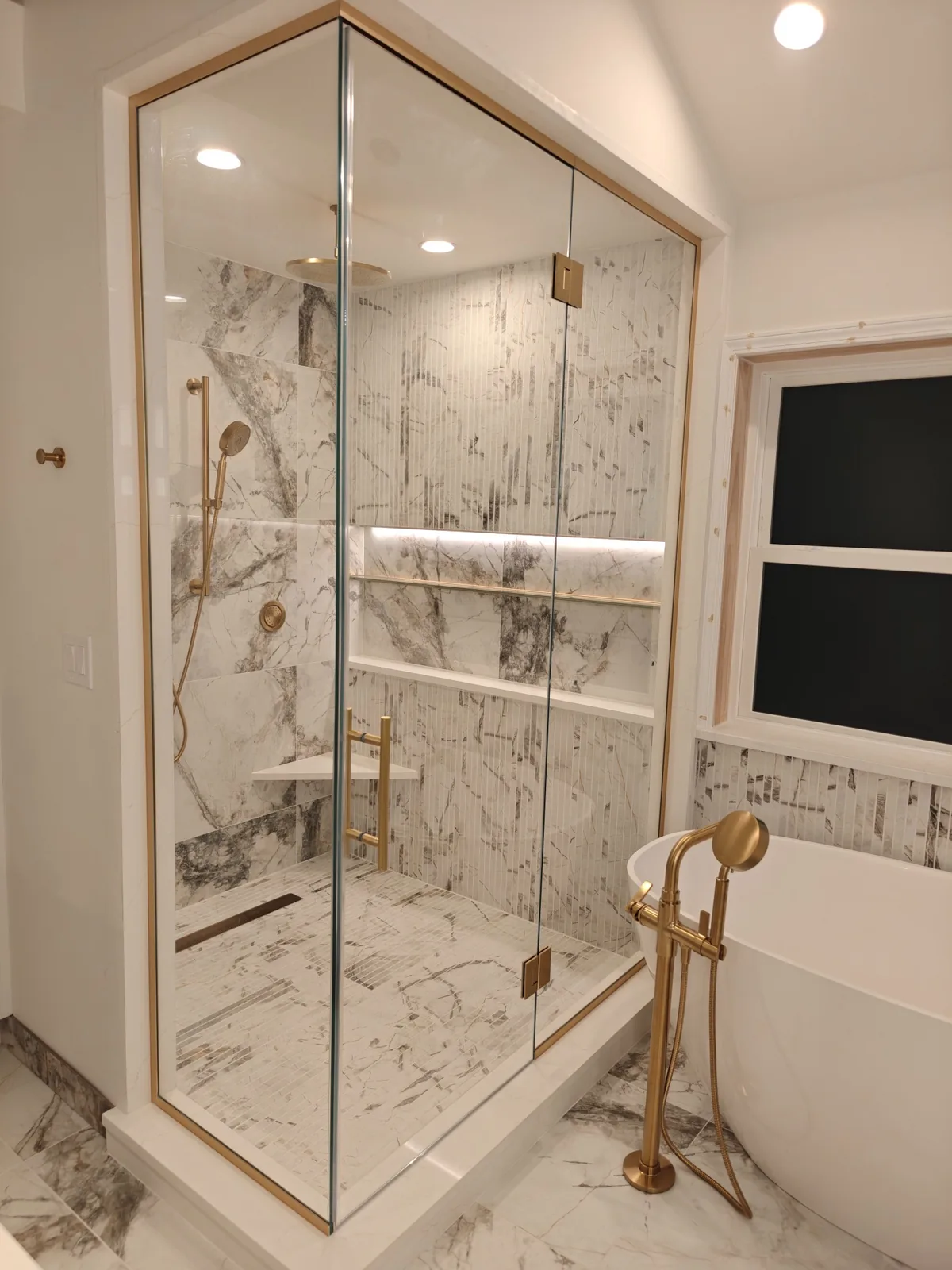 Corner view of a brass-framed shower with a frosted front panel, clear return glass and a gold-toned bathtub faucet.