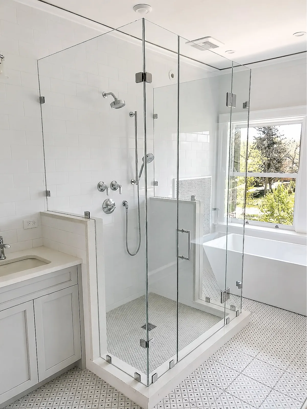 Full-height clear corner shower with a glass door between a white vanity and a sunlit bathtub.