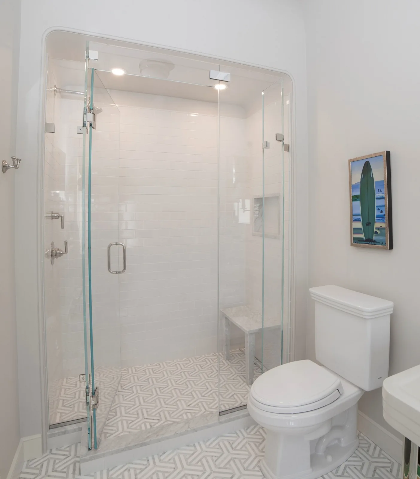 Clear glass shower door and fixed panel in a white bathroom with patterned floor tile.