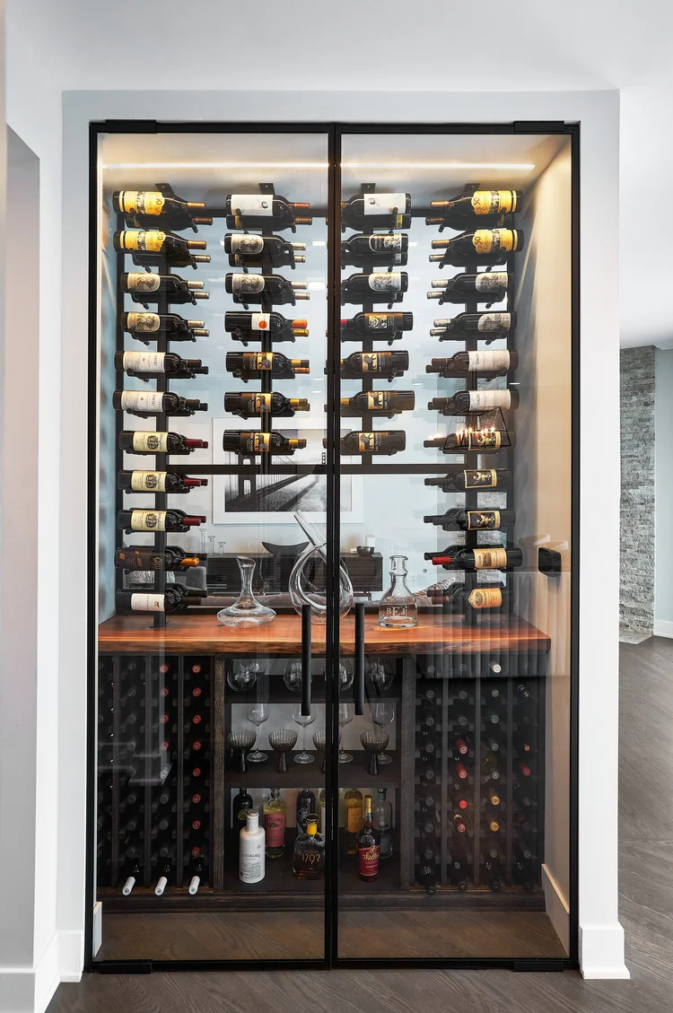 Black-framed double glass doors enclosing an illuminated wine display with a wood counter