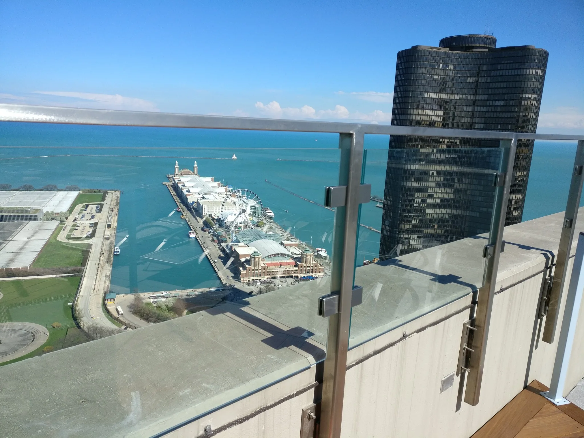 Clear glass railing with metal posts and a top rail overlooking the lake, Navy Pier and nearby high-rise buildings.