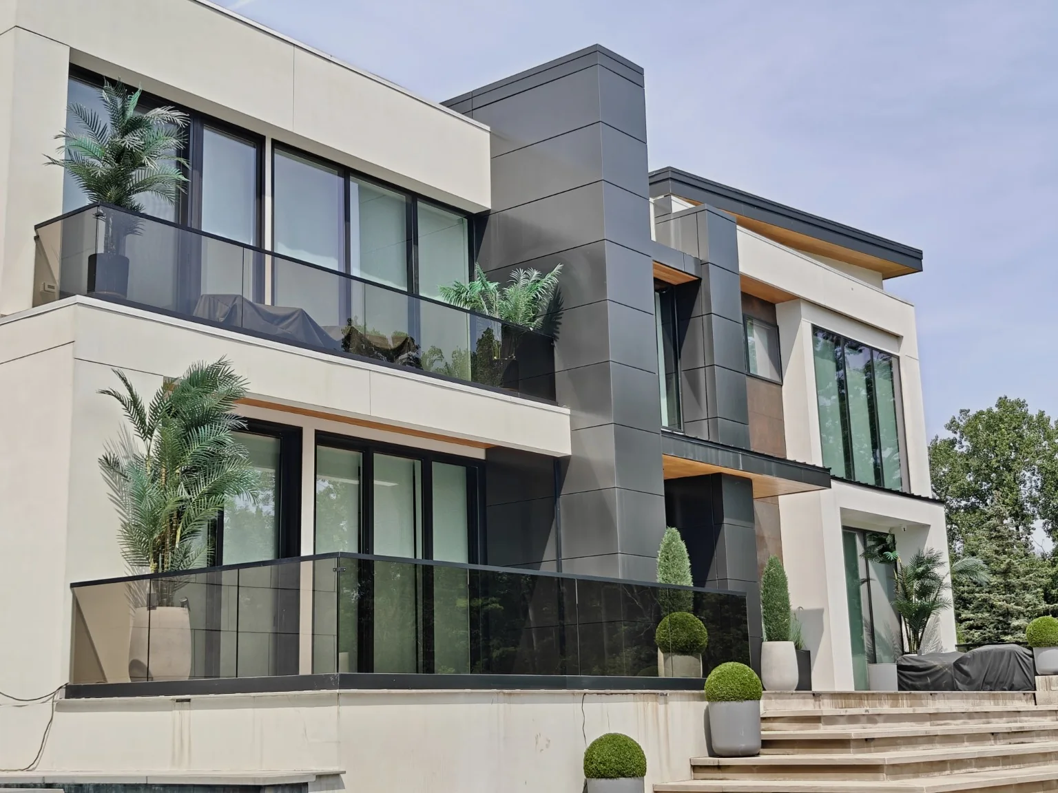 Dark glass balcony railings across two levels of a modern home with pale stone and charcoal cladding